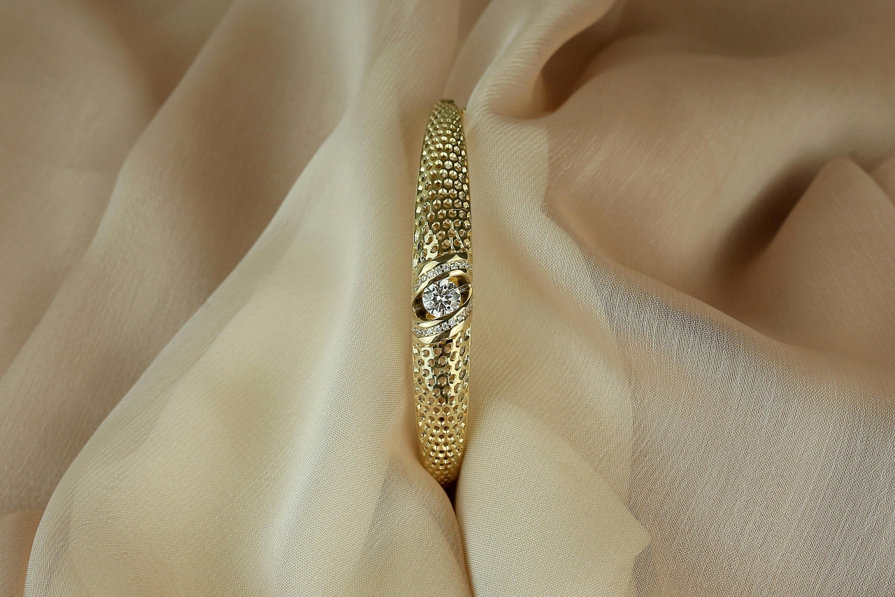 A yellow gold diamond engagement ring with a textured band on a piece of gauzy fabric.