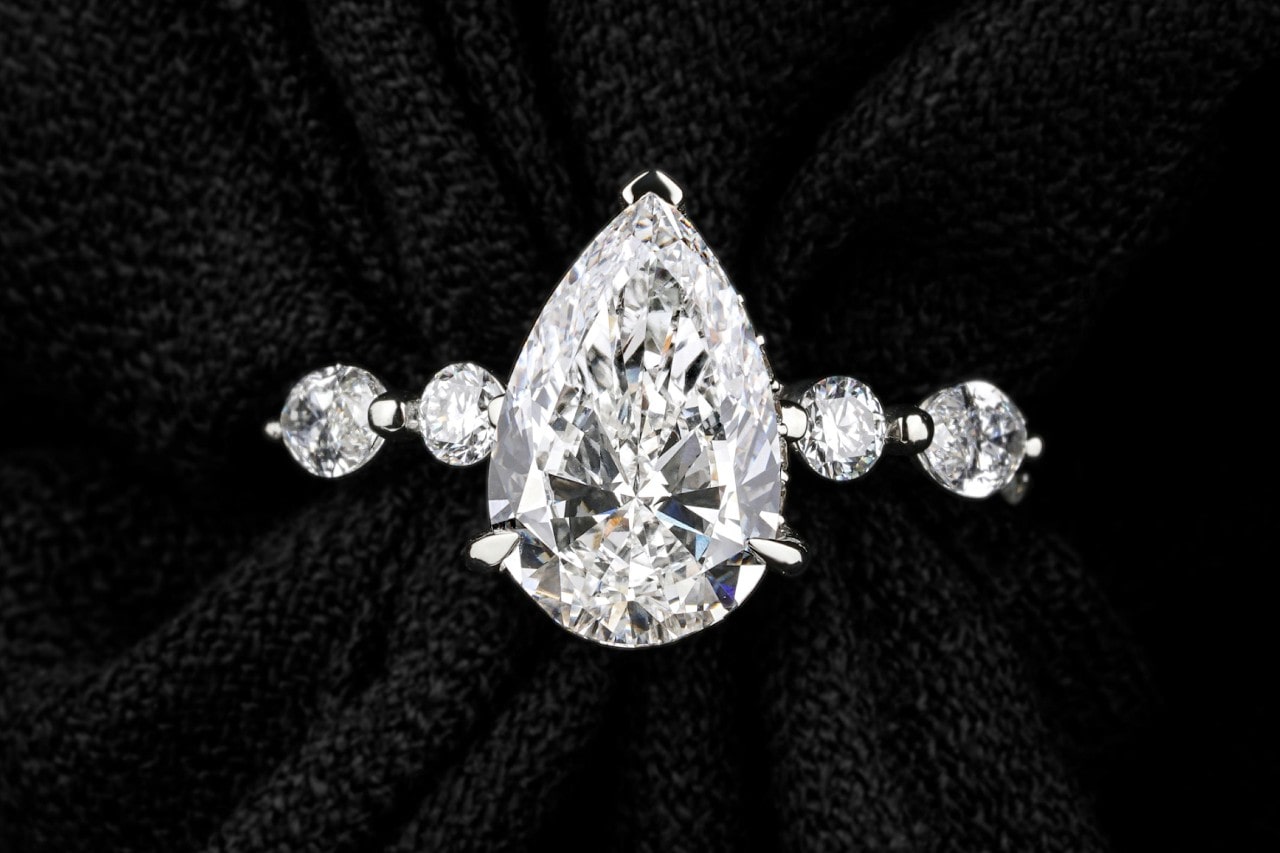 A close-up image of a pear shape engagement ring with round cut center stones.