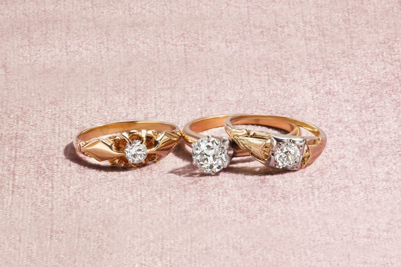 Three unique rose gold engagement rings with distinctive settings on a pale pink backdrop.