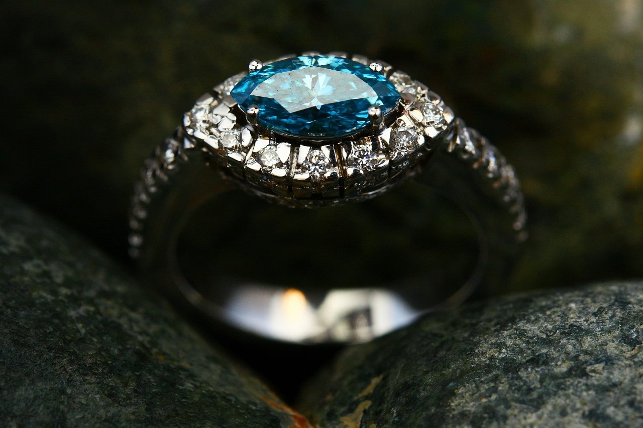 A close-up image of an engagement ring with a marquise cut, blue center stone.