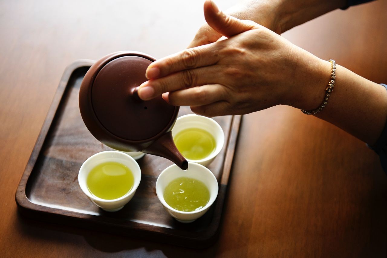 A woman wearing a diamond tennis bracelet pours green tea into cups