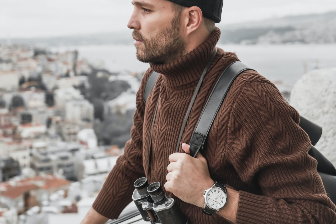 A man explores the outskirts of a village while wearing a watch.