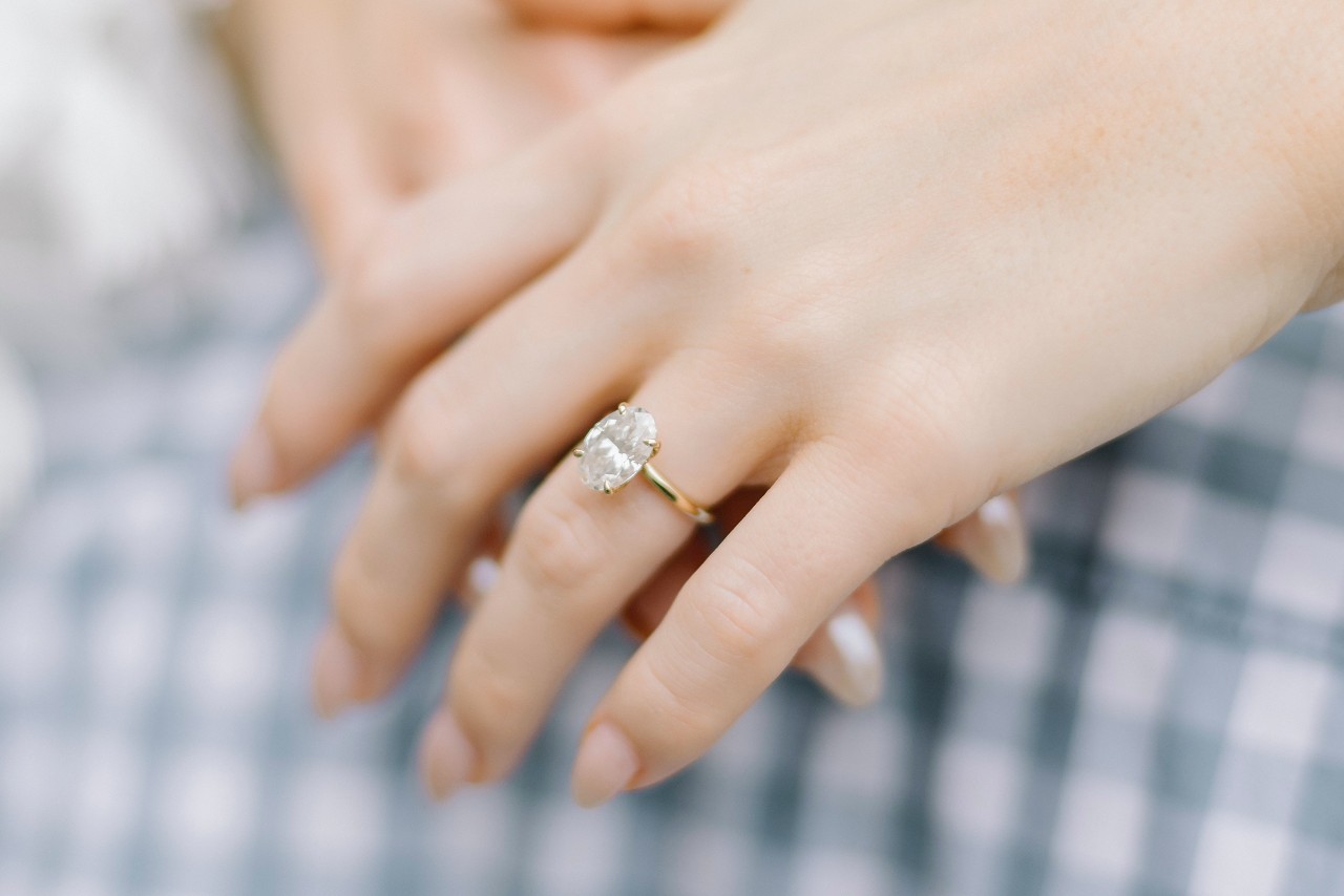 A close-up of a woman’s hands, a simple solitaire engagement ring adorning her finger.