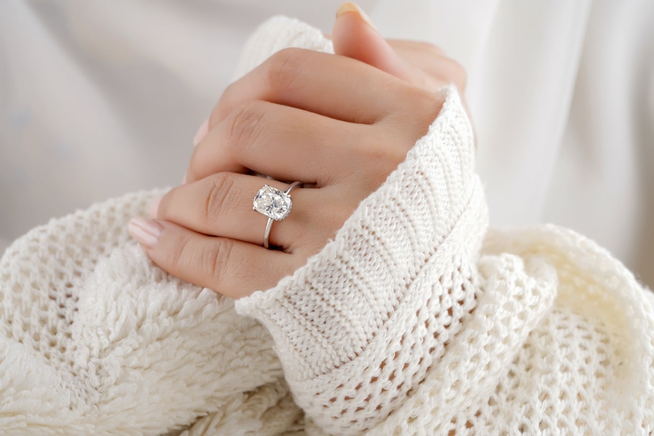 A close-up of a woman wearing a comfortable sweater, a solitaire engagement ring adorning her finger.