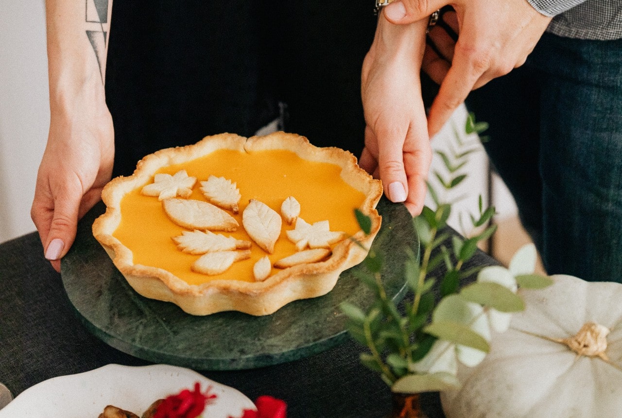 A close-up of a couple preparing a pumpkin pie, a bold bracelet on her right wrist.