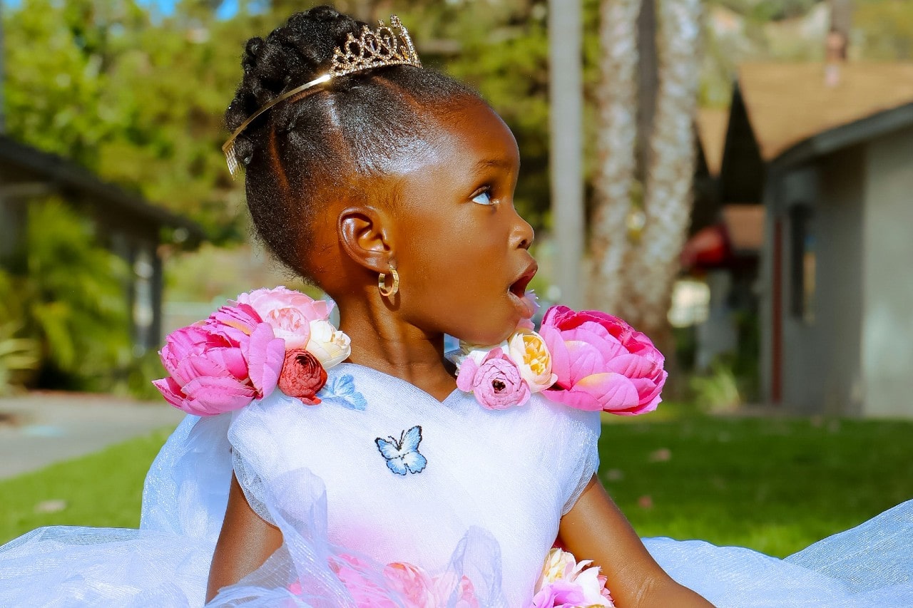 A little girl in a tulle princess dress and wearing gold earrings looking off-camera.