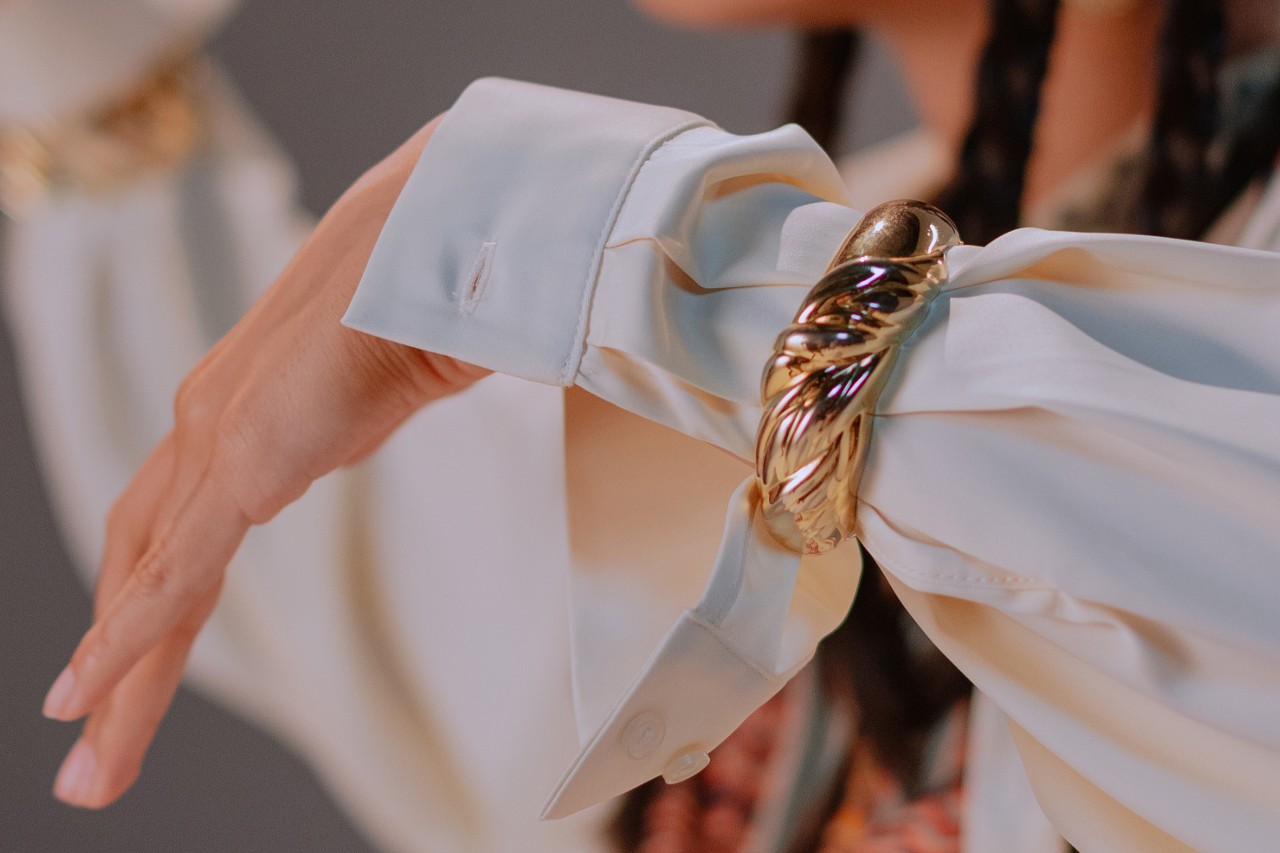 a woman’s arm adorned with a large, bold yellow gold sculptural bracelet