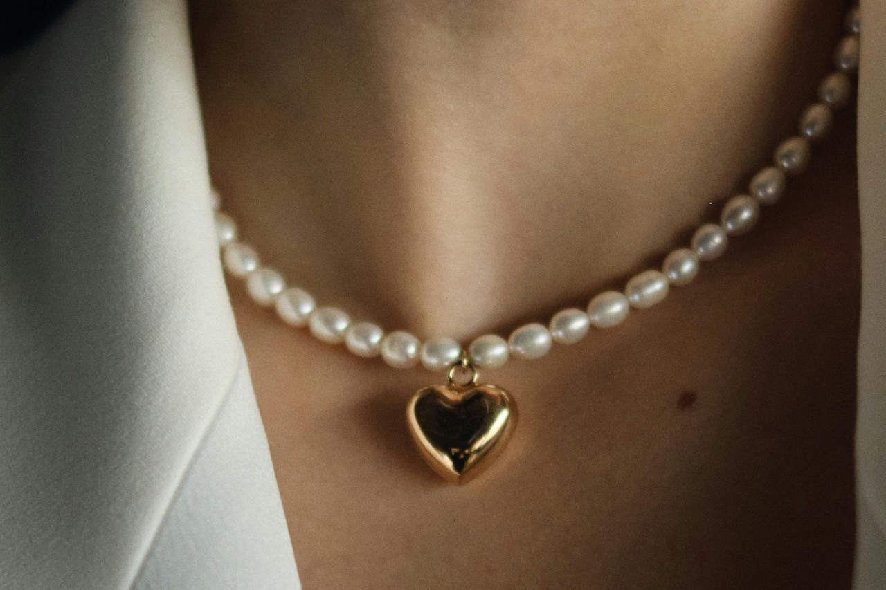 close up image of a woman’s neck adorned with a pearl and heart pendant necklace