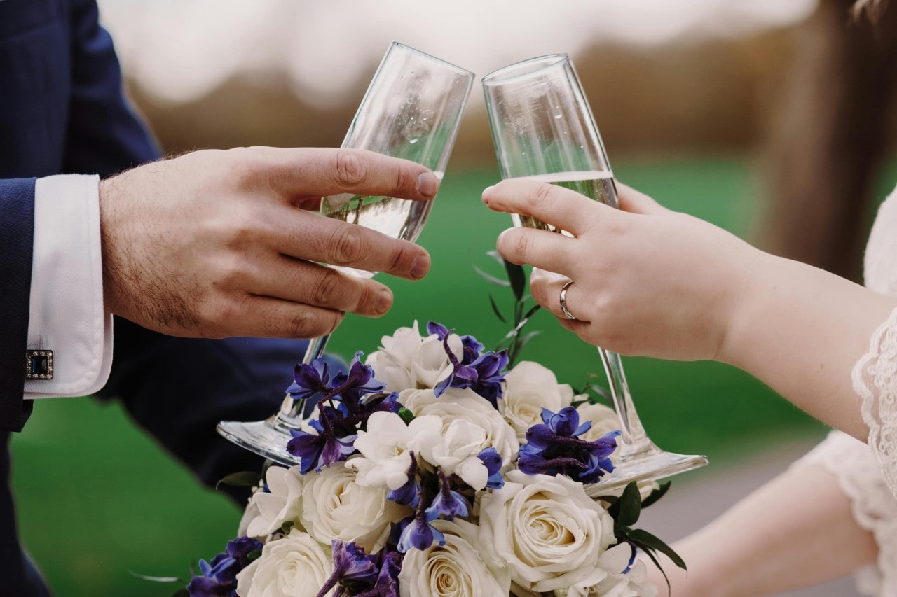 A newlywed couple toasting champagne flutes over the bouquet.