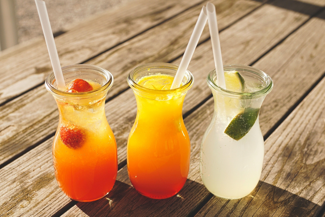 A close-up of three colorful cocktails on a wooden deck.