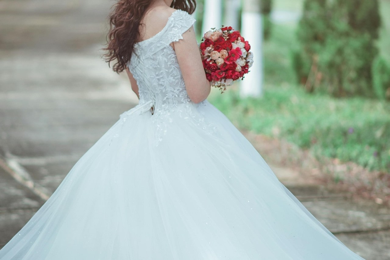 A close-up of a bride wearing a classic wedding dress, holding a red bouquet.