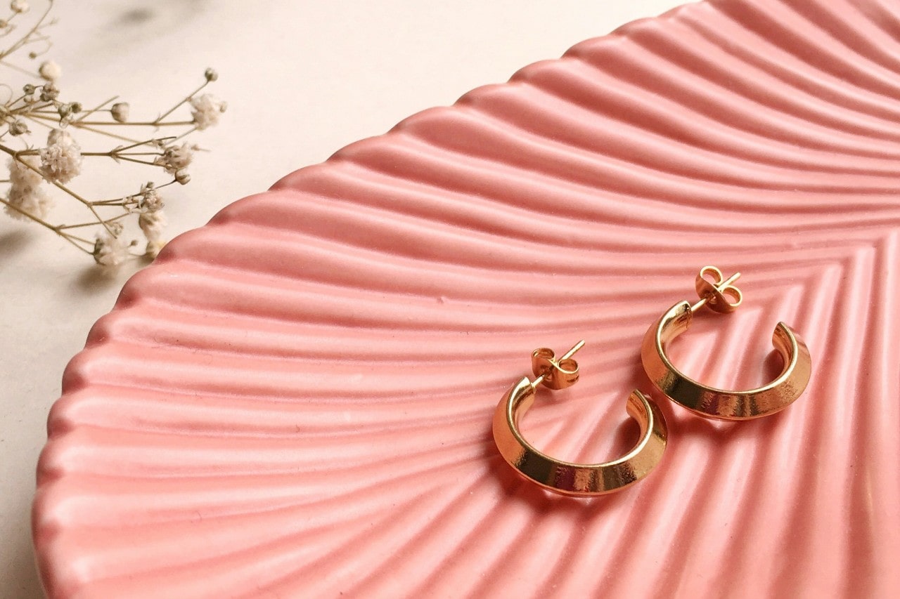 a pair of yellow gold huggie earrings on a pink dish