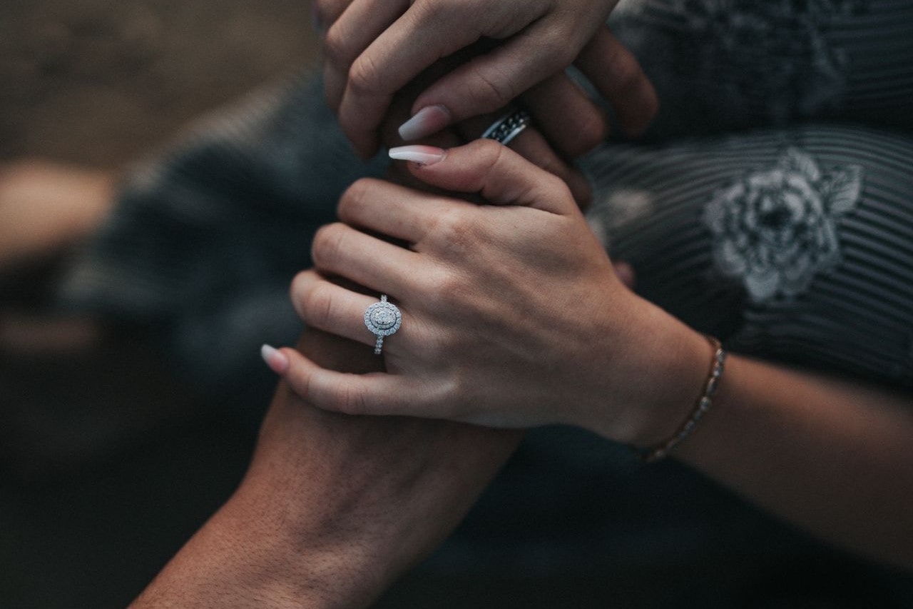 a couple holding hands, the woman wearing an oval cut halo set engagement ring