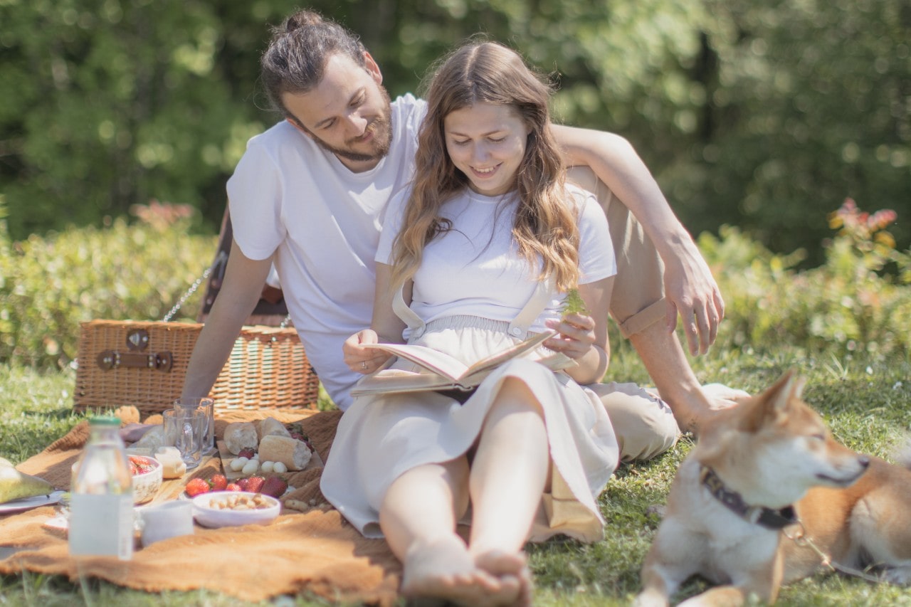 a couple having a picnic with their dog in a park and reading a book together