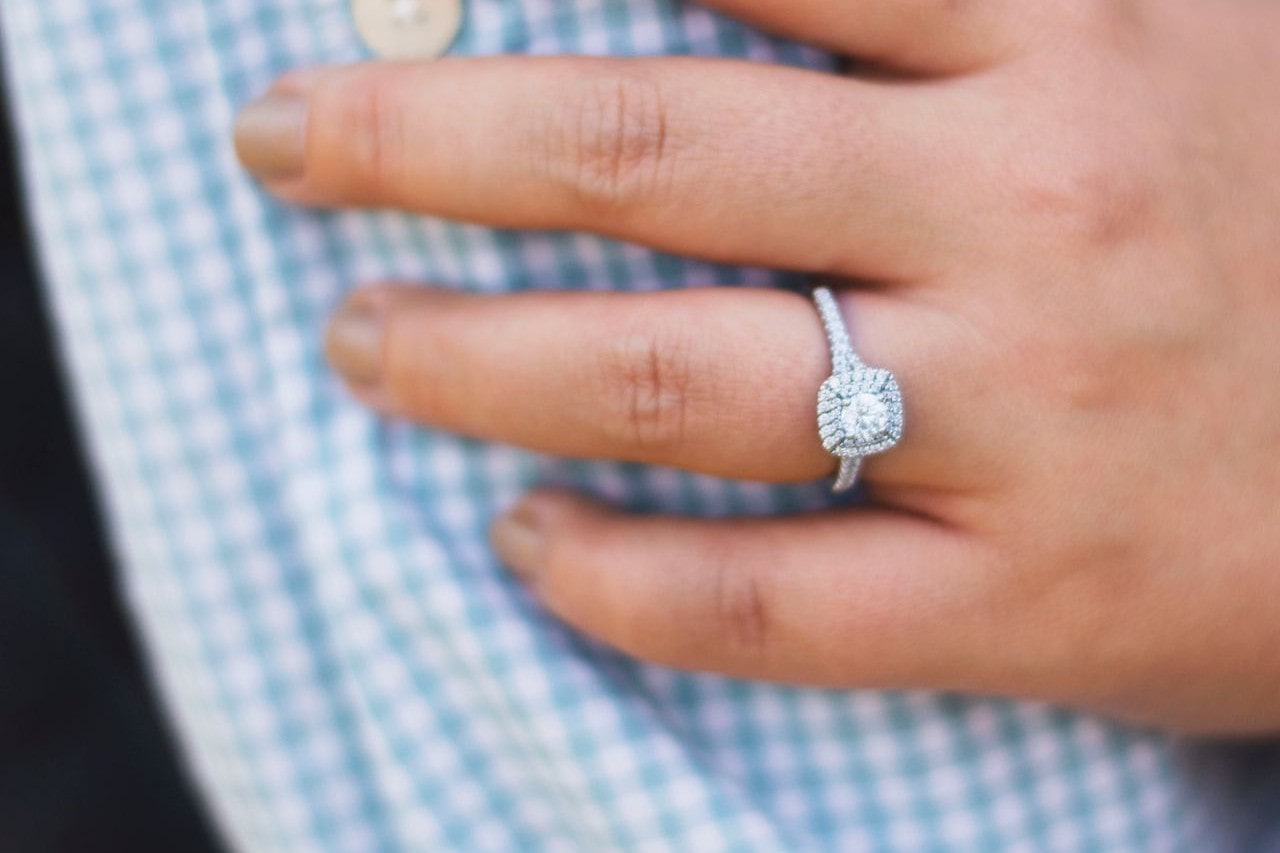 a woman’s hand on a man’s arm wearing a white gold halo engagement ring