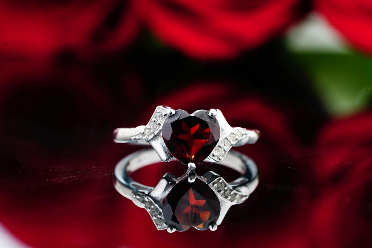 a heart shaped ruby engagement ring on a reflective surface