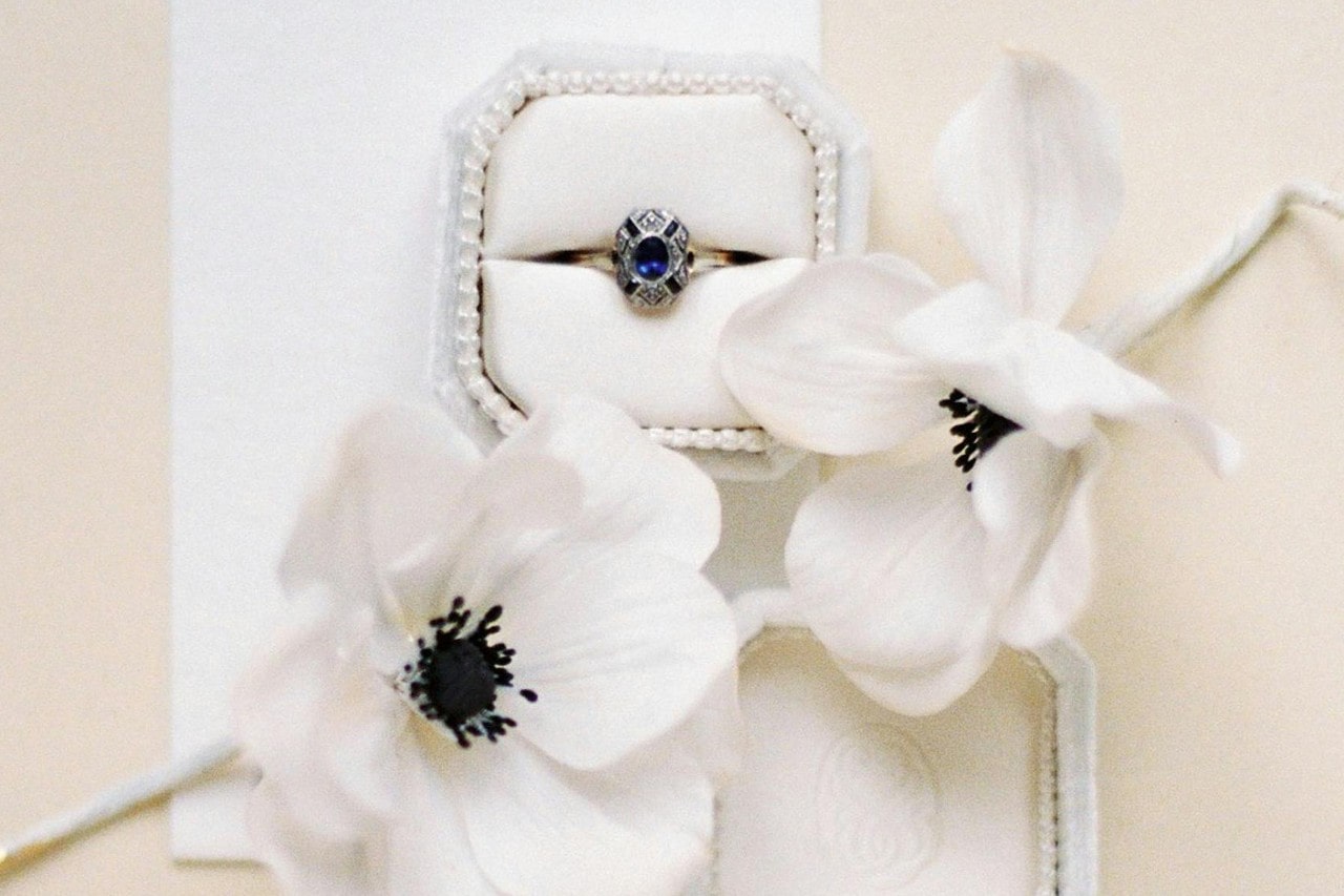 a sapphire engagement ring in a white box surrounded by white flowers