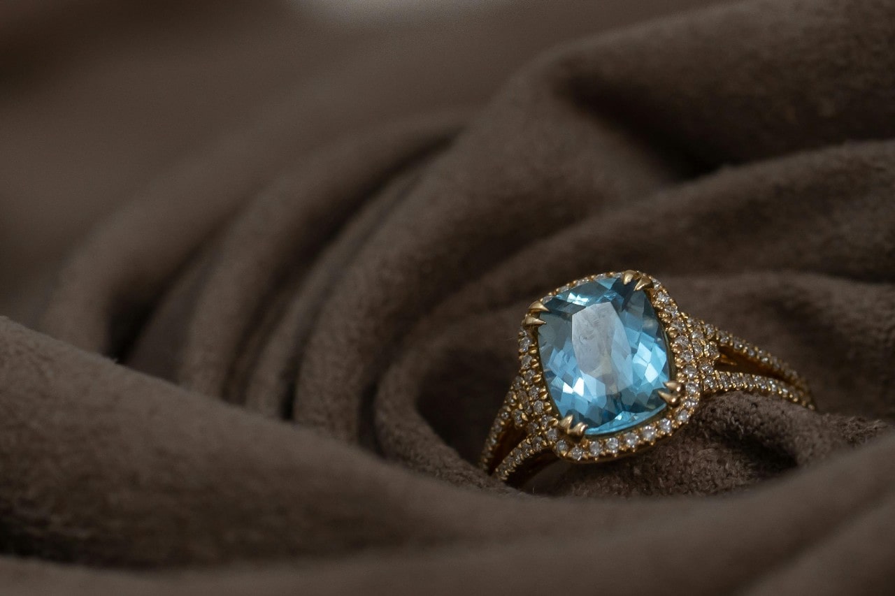 an aquamarine engagement ring with side stones sitting on a piece of brown cloth