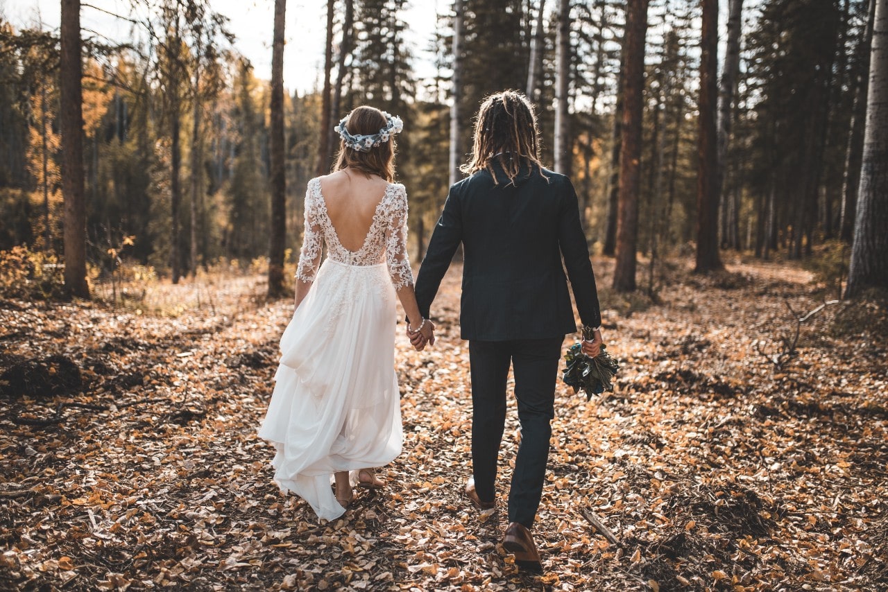 A young couple, backs facing the camera, having a minimalist wedding in a forested area.