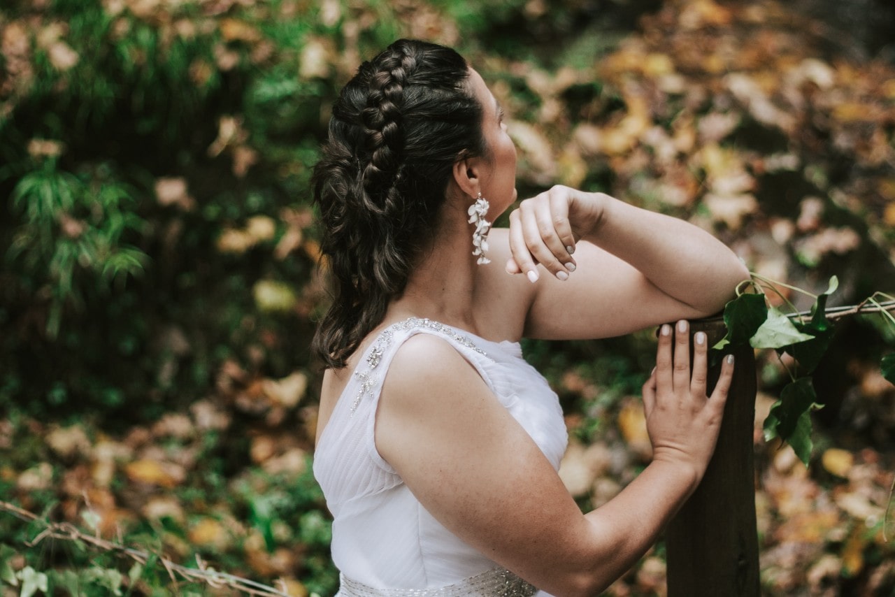 A young bride looking away from the camera, standing in a lovely clearing of autumn leaves.