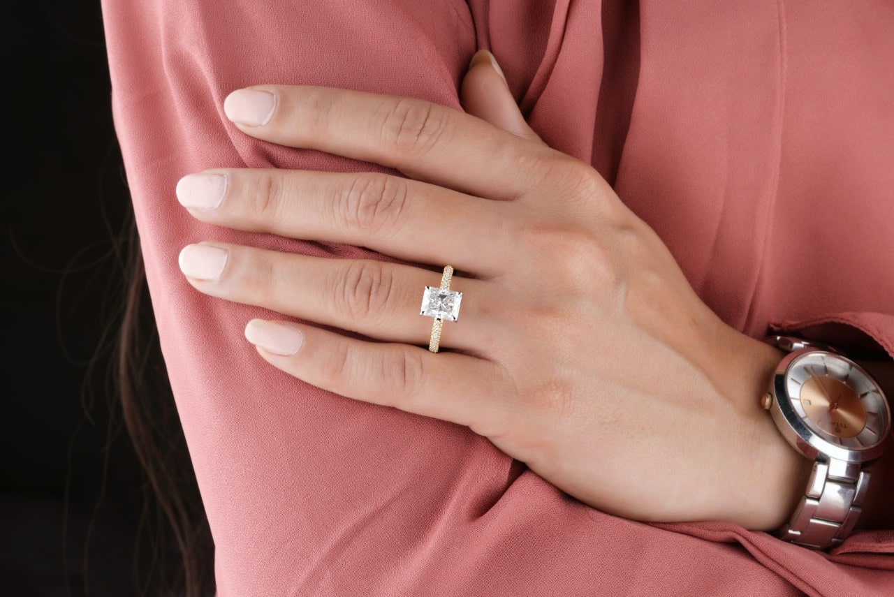 a woman’s hand resting on her arm and wearing an emerald cut engagement ring