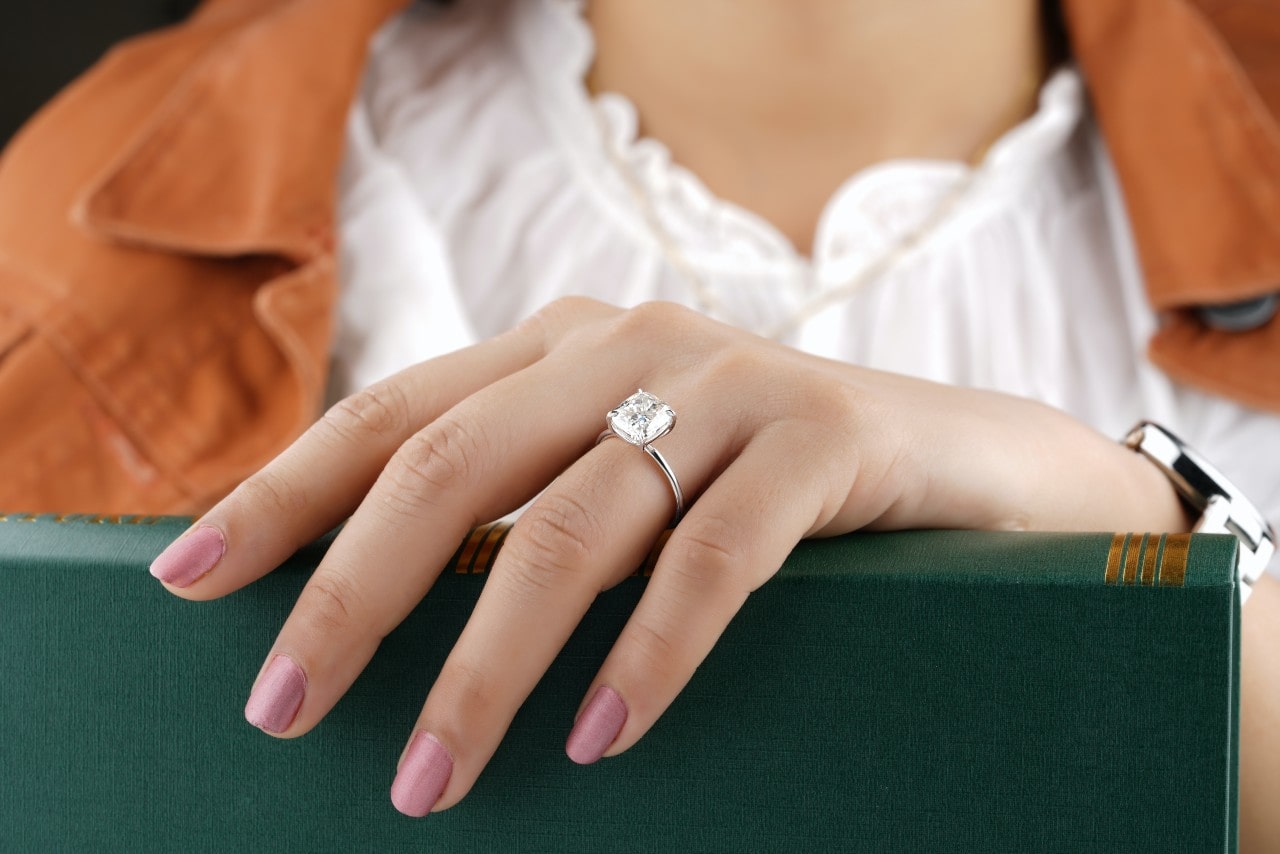 a woman’s hand resting on a green book wearing a solitaire engagement ring