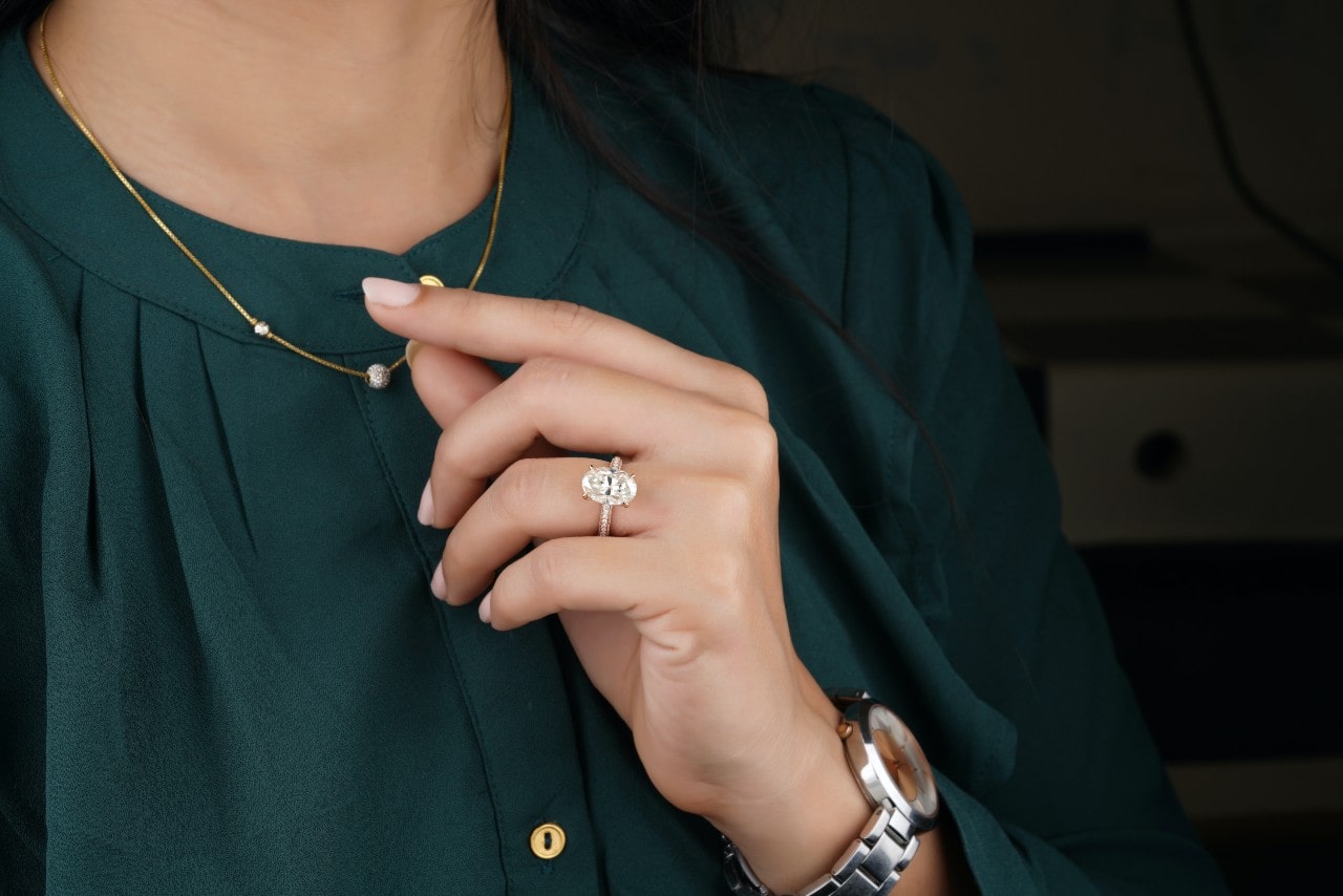 a woman’s hand holding her necklace and wearing an oval cut engagement ring