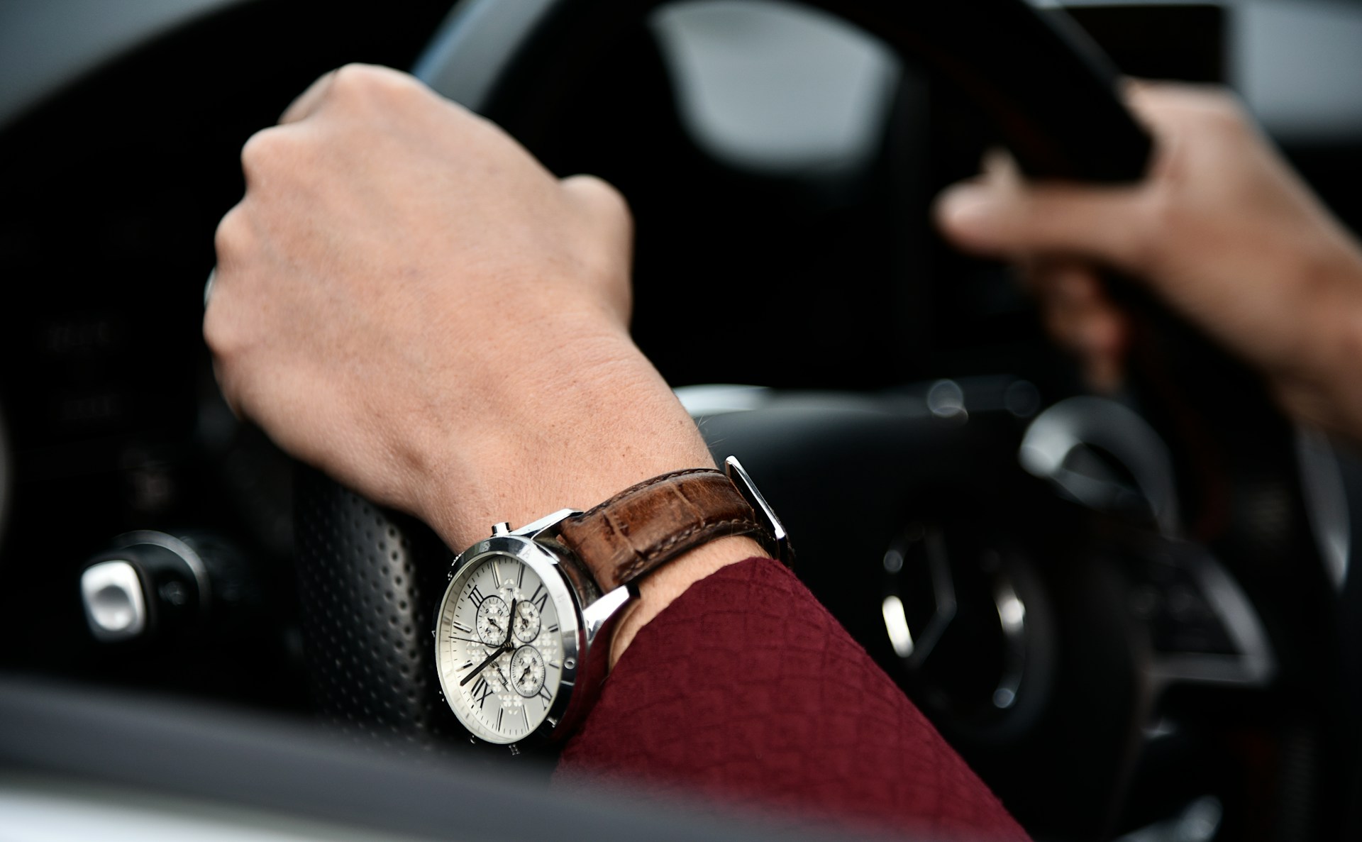 a person with their hands on a steering wheel, wearing a white and silver watch