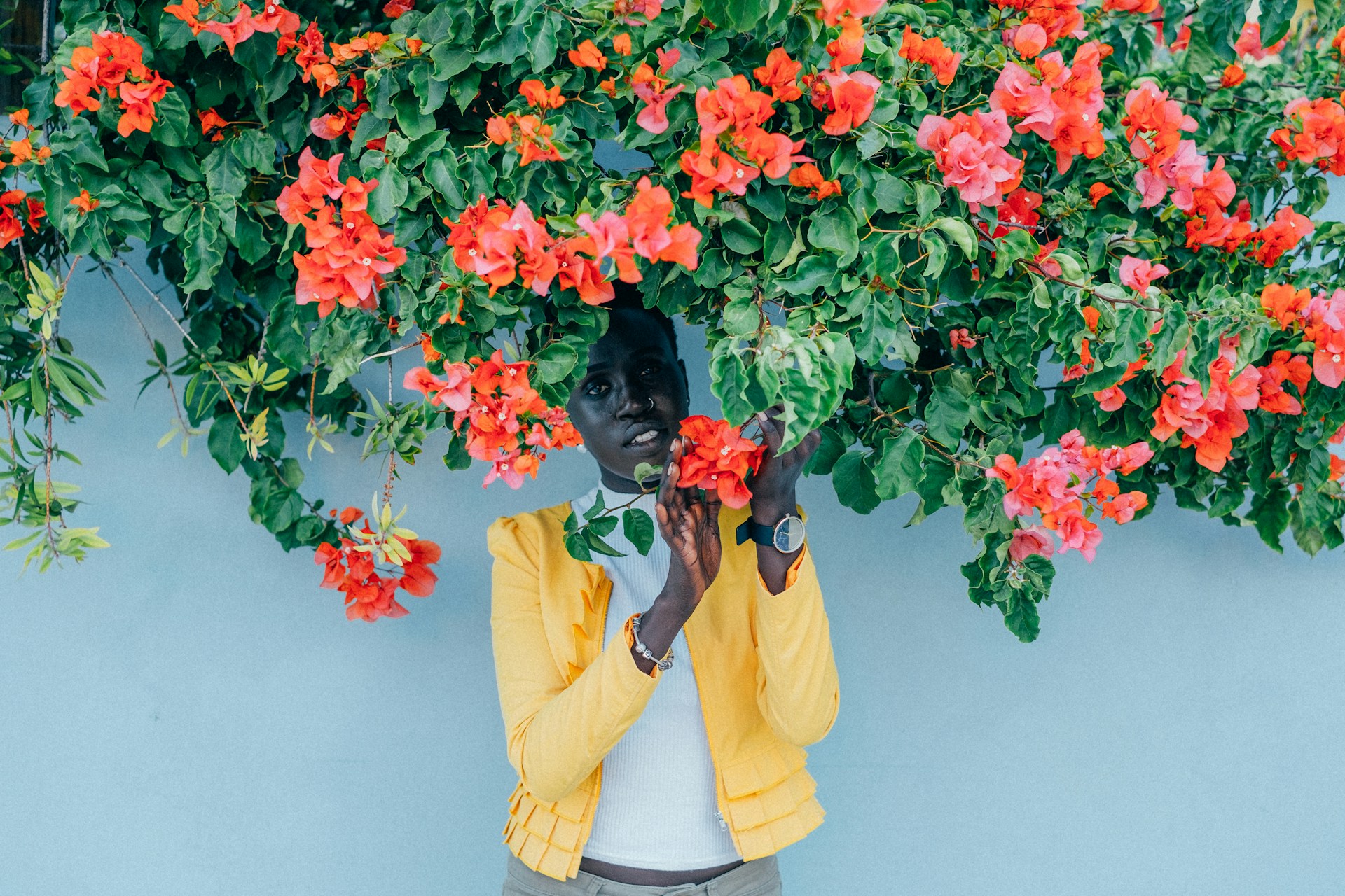 a woman in a yellow jacket standing under a canopy of flowers wearing a watch