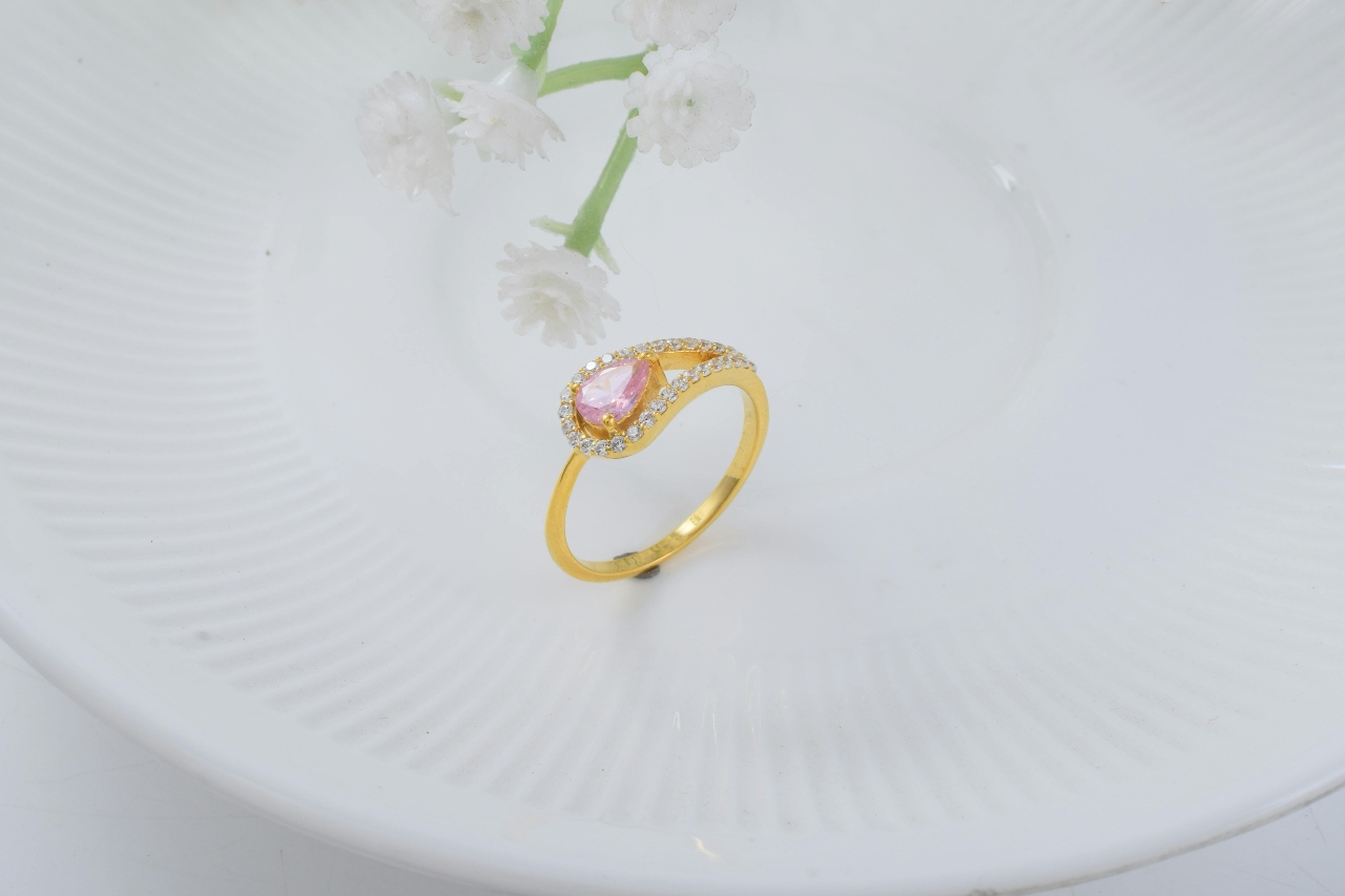 A unique split shank ring with a pink center stone displayed on a textured plate.