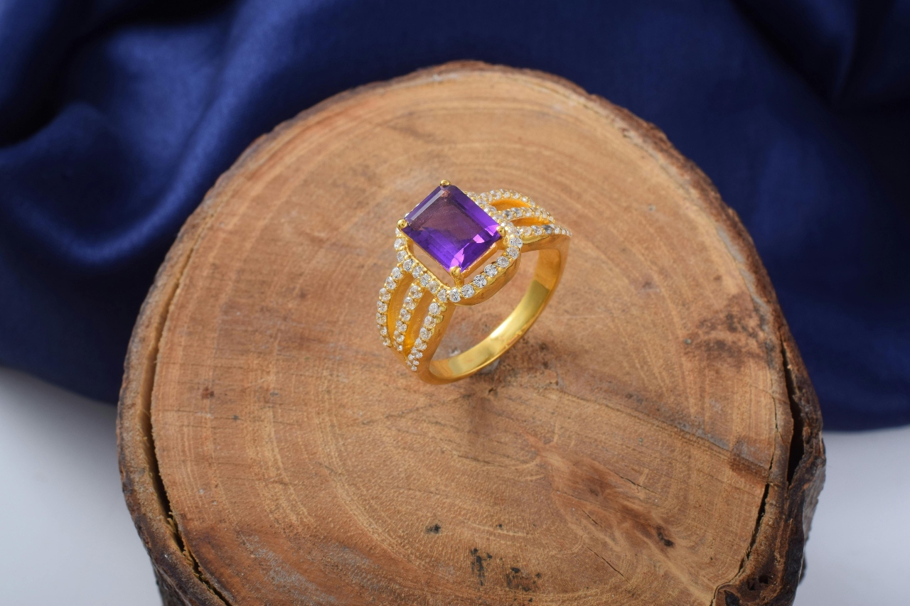 A yellow gold split shank ring with an amethyst center stone displayed on a wooden surface.