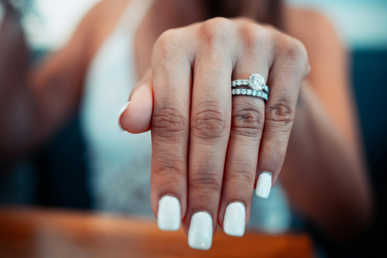 a woman putting her hand forward, displaying a diamond engagement ring and wedding band