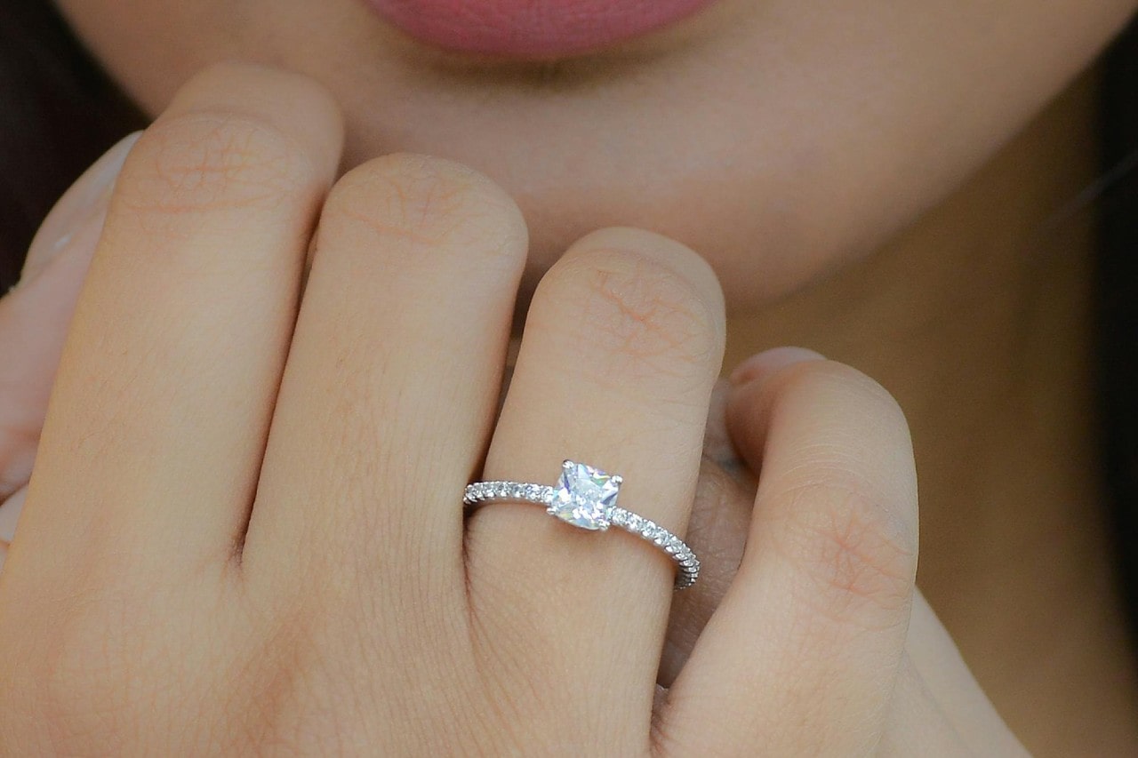 a woman holding her hand up to her face wearing a princess cut engagement ring