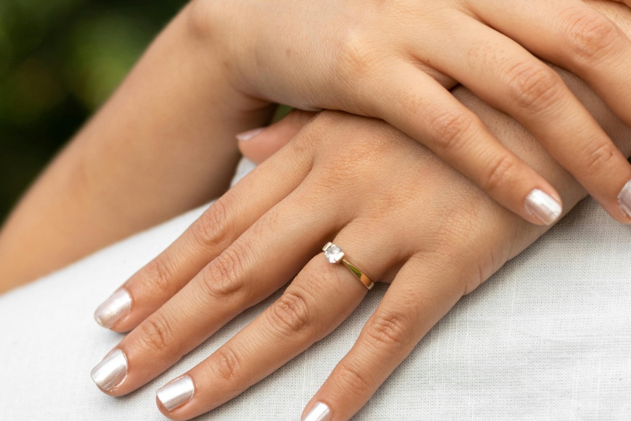 a woman’s hand crossed behind a man’s shoulders, wearing a yellow gold engagement ring