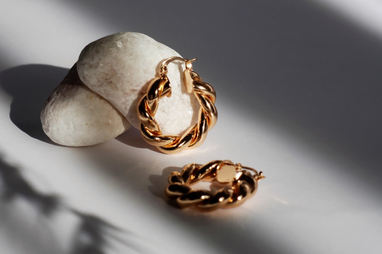 a pair of hello gold huggies earrings lying on a white surface, propped against white rocks