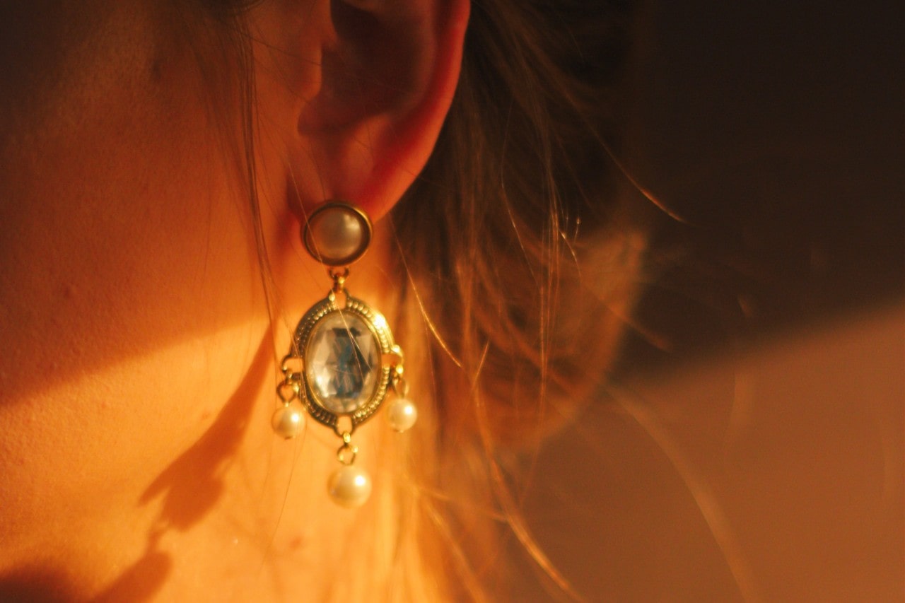 Close up of person wearing an oval-shaped earring with three dangling pearls