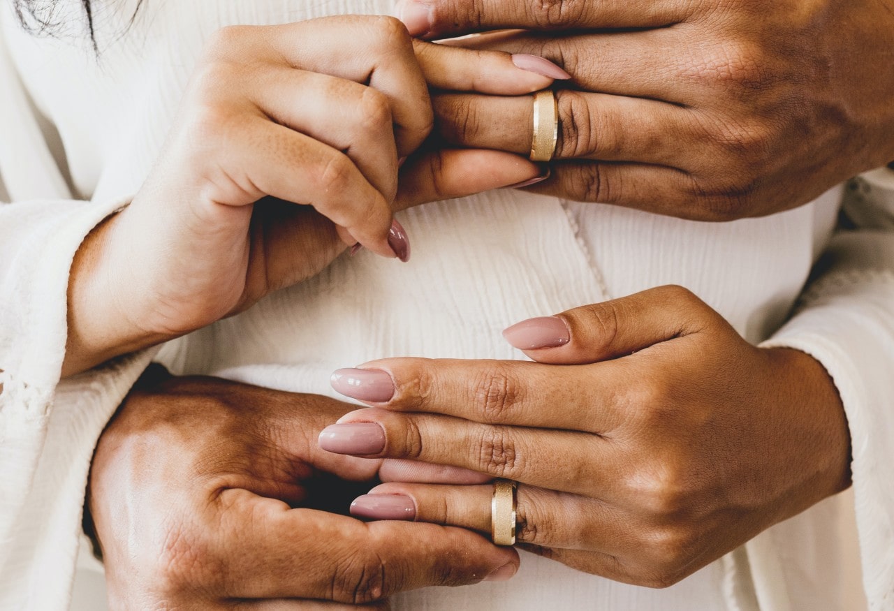 A man and woman placing matching yellow gold wedding bands on each other’s fingers