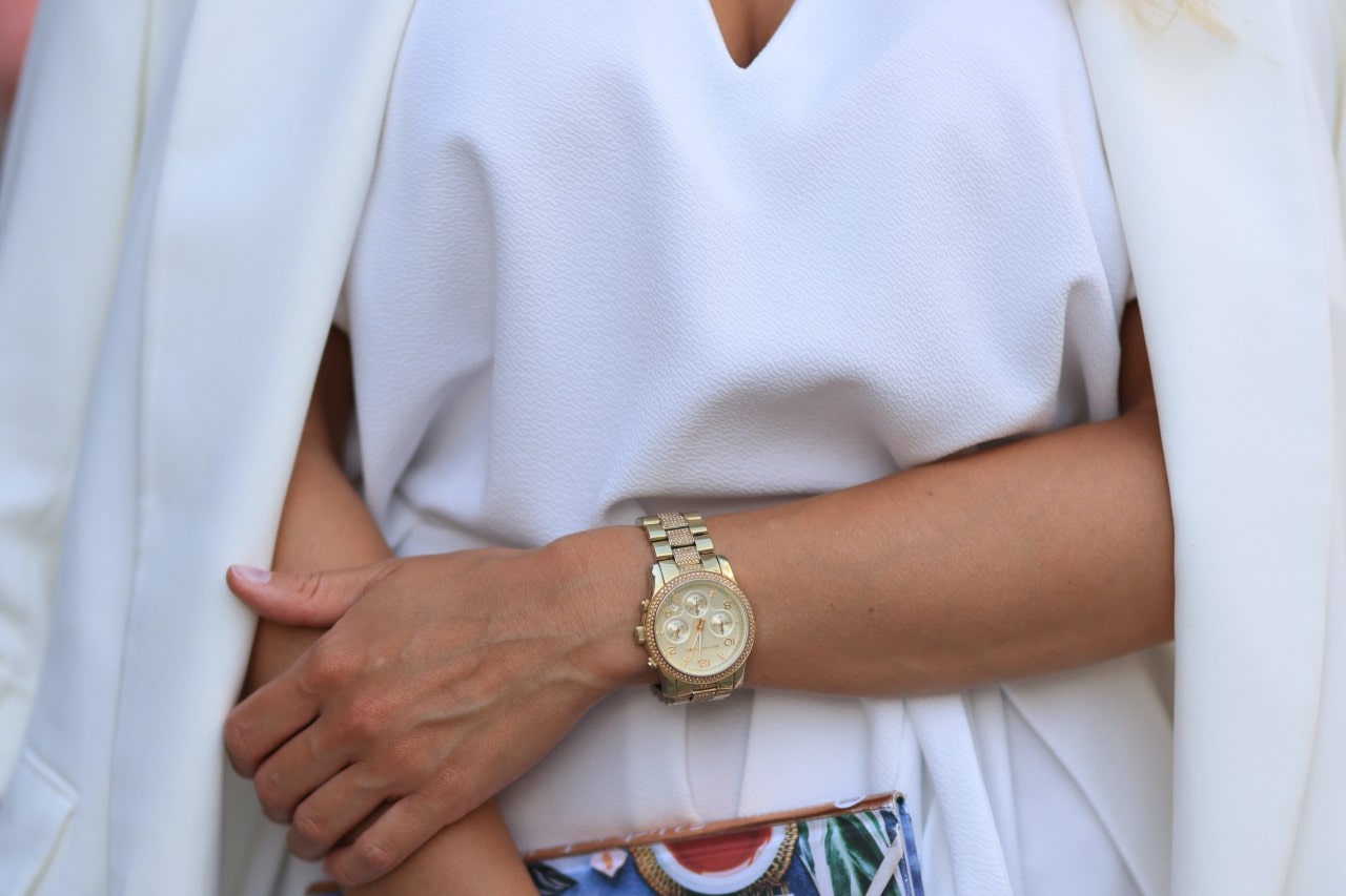 Close up of a gold watch on a woman wearing white and holding a colorful clutch