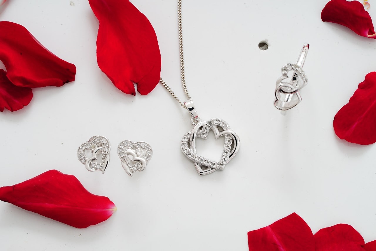 A set of silver and diamond heart-shaped jewelry surrounded by rose petals