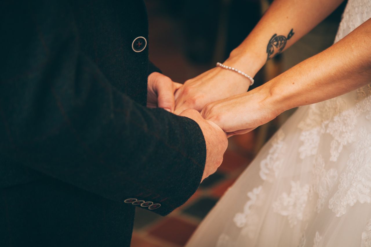 A single diamond bracelet on the wrist of a bride holding hands with her groom