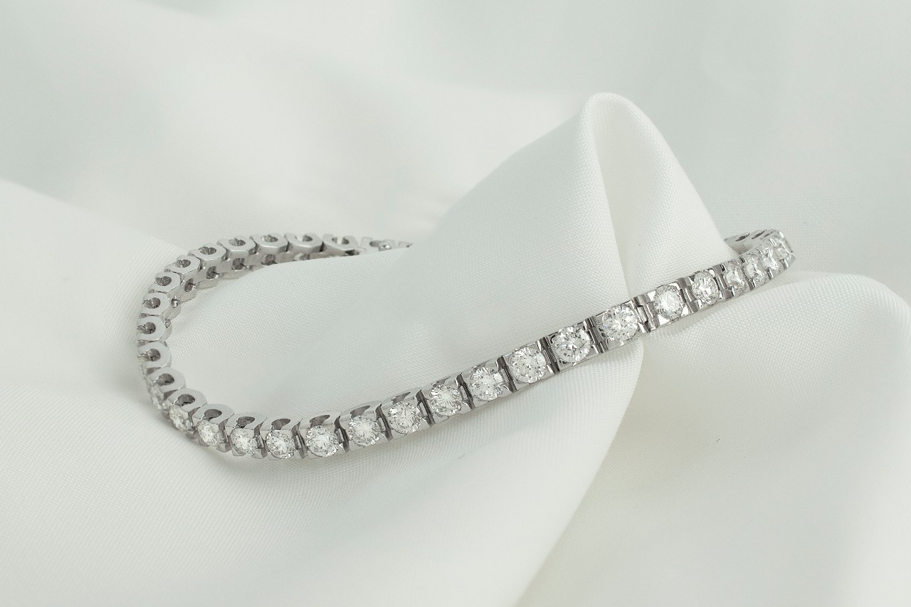 A silver diamond tennis bracelet lying on a crisp white cloth