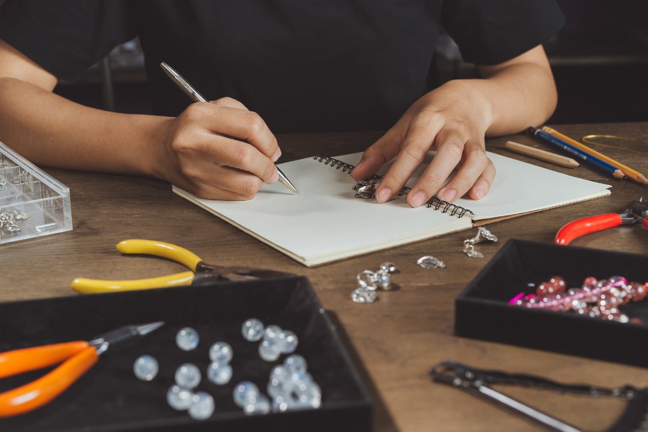 A young jewelry designer sketches a design inspired by a vintage brooch in his workshop