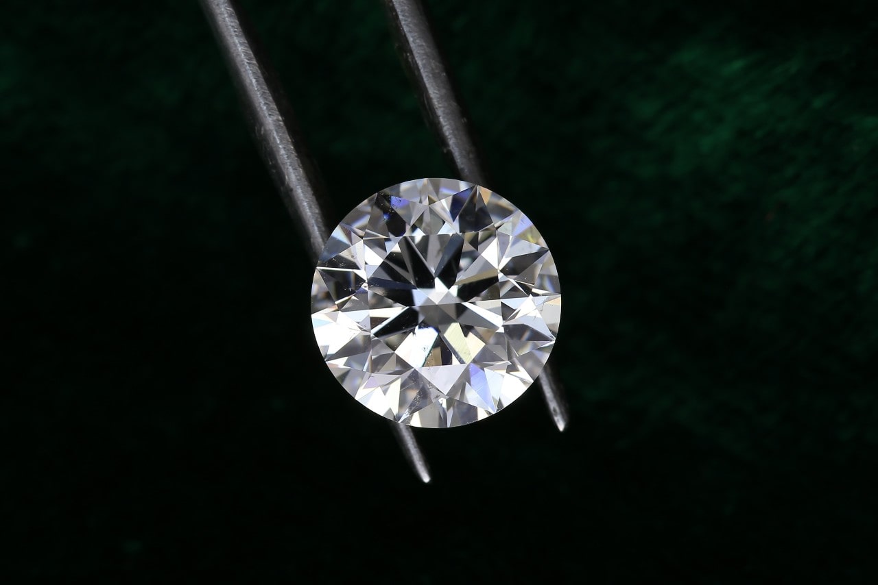 A jeweler holds a diamond in his tweezers as he observes it against a dark green background