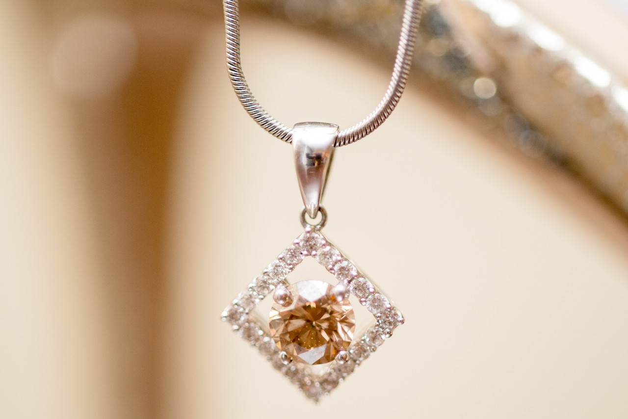 A necklace featuring a gemstone is framed by a tilted diamond square dangling over the edge of a bedroom dresser