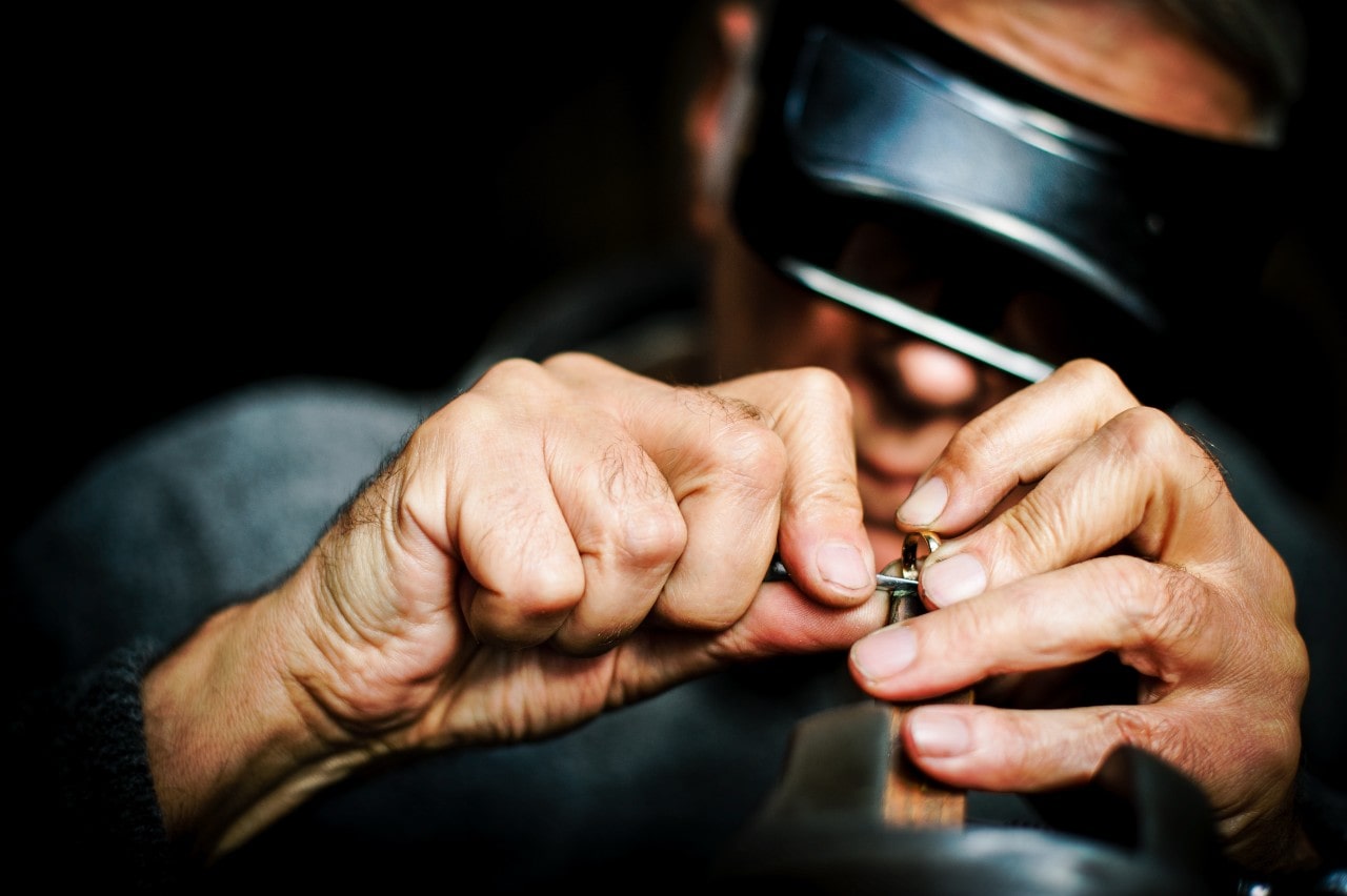 A jeweler works on a broken piece of gold jewelry in his dark workshop