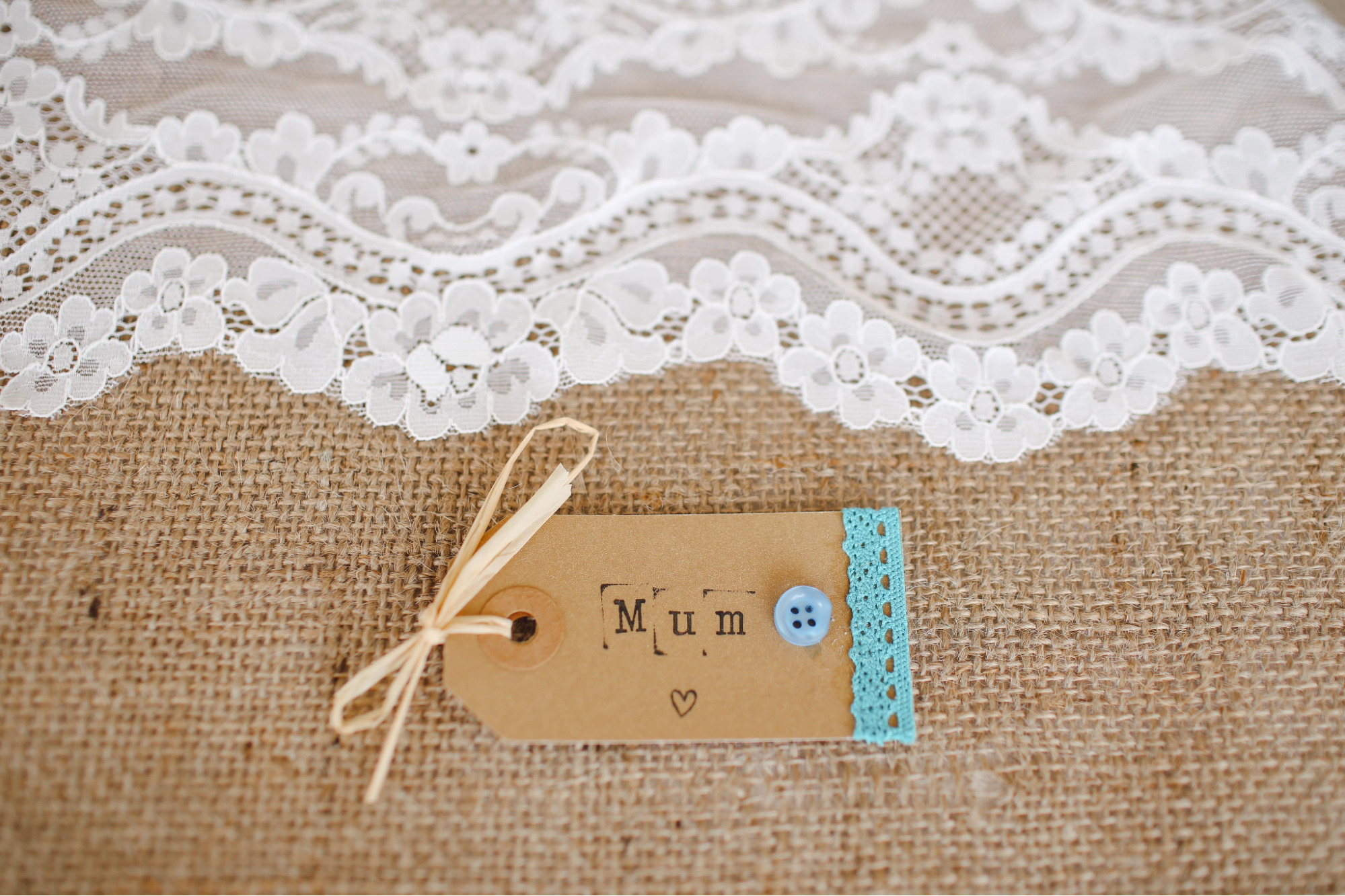 A homemade gift tag for a mother sits on a burlap and lace table runner