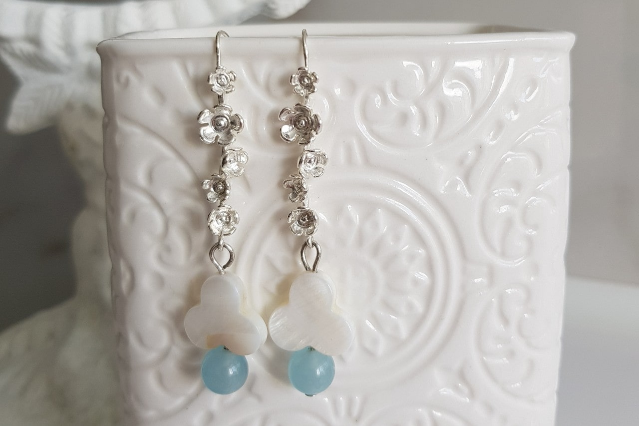 A pair of sterling silver drop earrings featuring flowers and gemstones hang on a ceramic cup