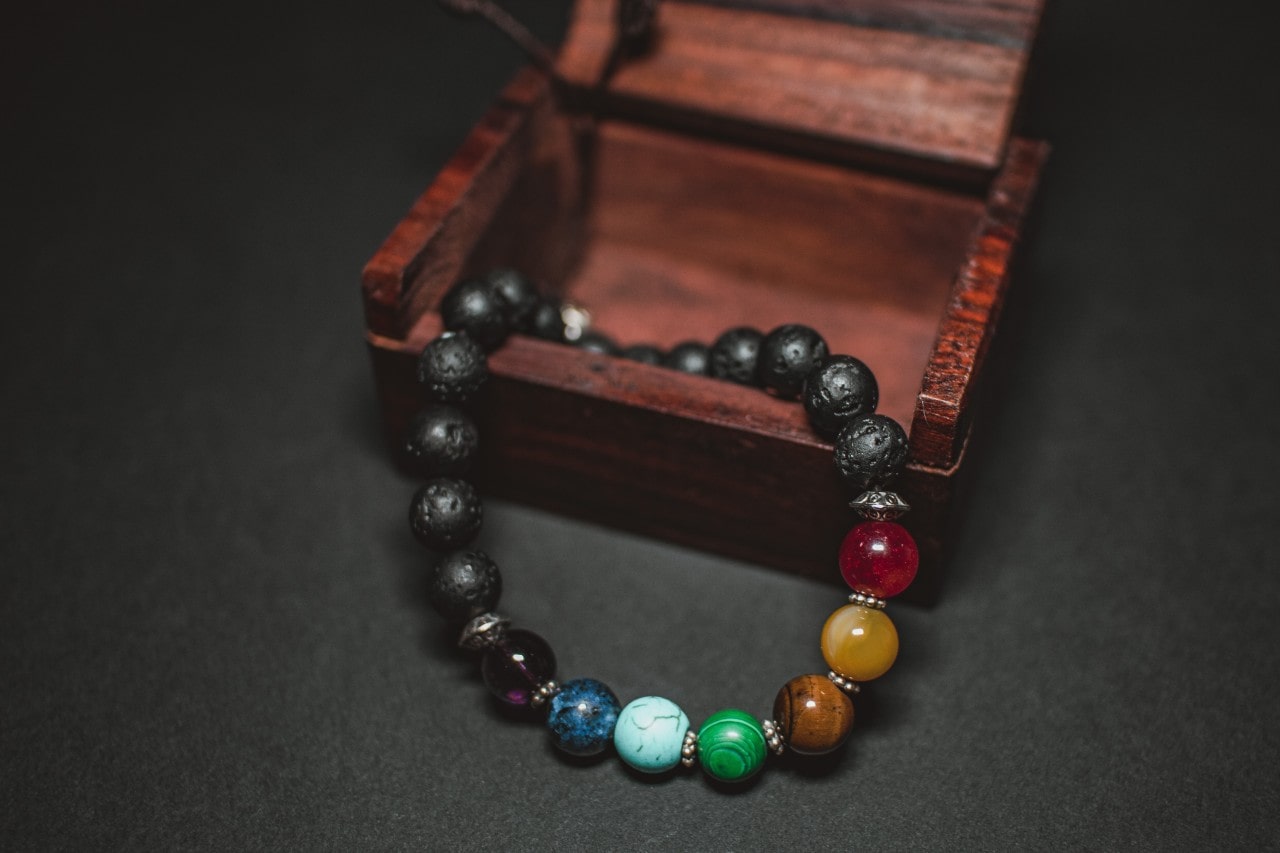 A gemstone beaded men’s bracelets sit at the base of a wooden tiered tray jewelry organizer