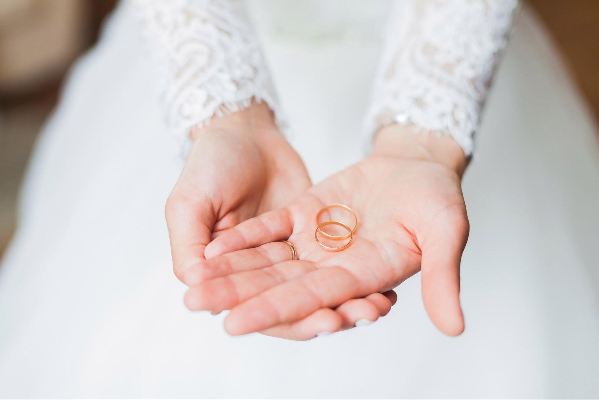 Rose gold wedding bands held by a bride.