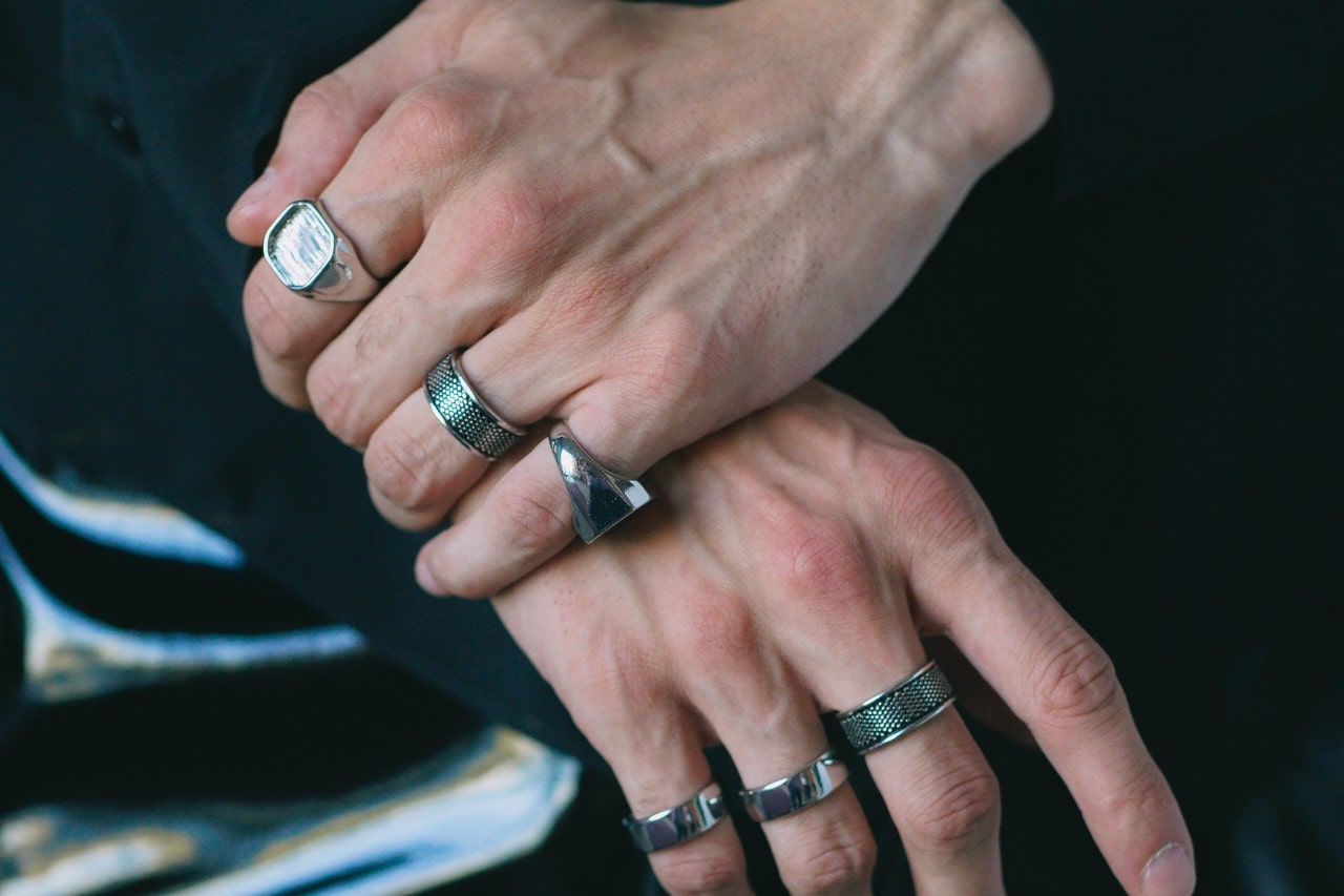 Man’s hands crossed over one another, wearing six silver rings.